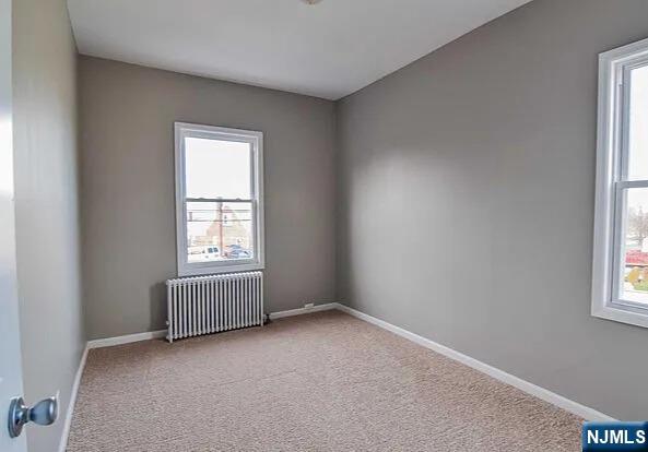 carpeted empty room featuring baseboards and radiator