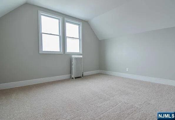 additional living space with carpet floors, baseboards, lofted ceiling, and radiator heating unit