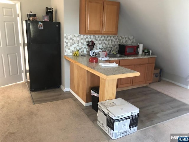 kitchen with light countertops, a peninsula, tasteful backsplash, a sink, and freestanding refrigerator