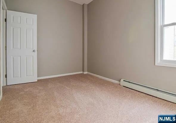 carpeted empty room featuring baseboards, vaulted ceiling, and baseboard heating