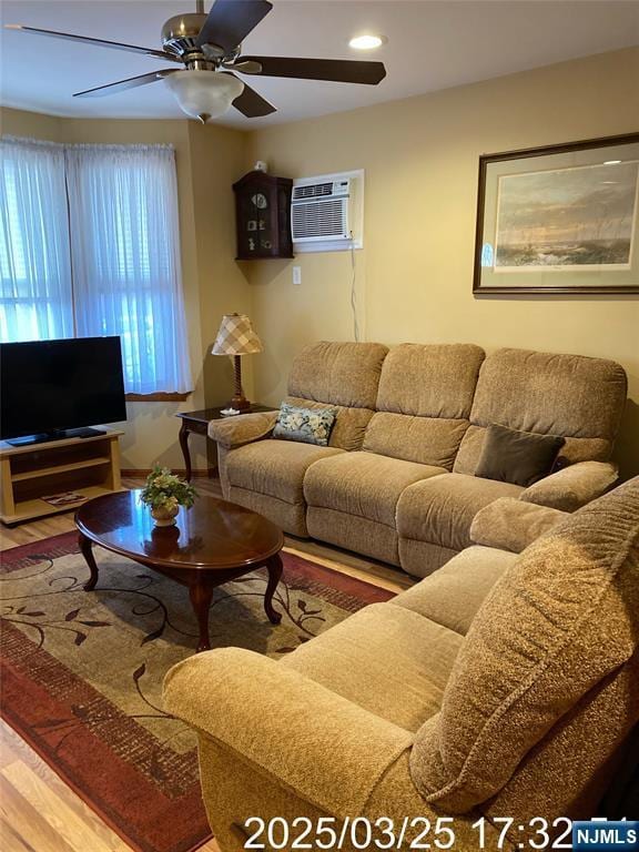 living room with ceiling fan, wood finished floors, and an AC wall unit
