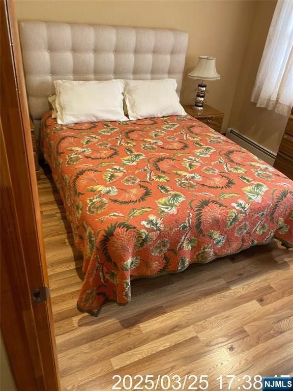 bedroom with wood finished floors and baseboard heating