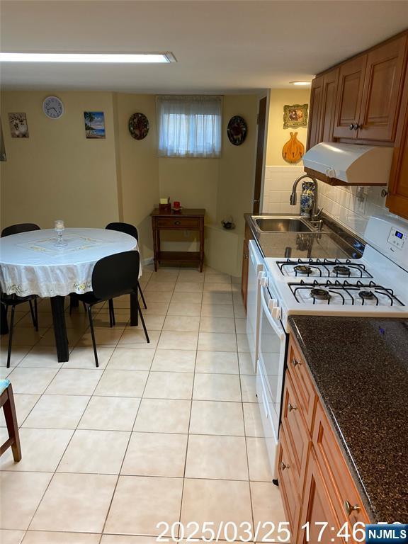 kitchen with brown cabinets, under cabinet range hood, a sink, white gas range oven, and light tile patterned floors