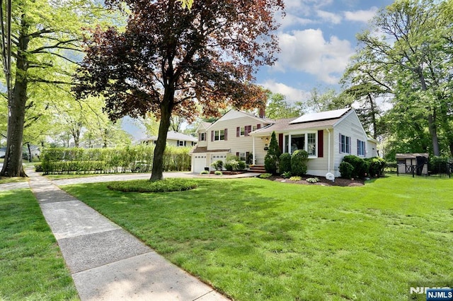 split level home featuring an attached garage, roof mounted solar panels, a front yard, and driveway