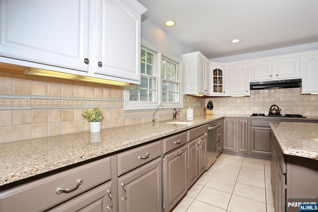 kitchen with under cabinet range hood, a sink, dishwasher, gray cabinetry, and decorative backsplash