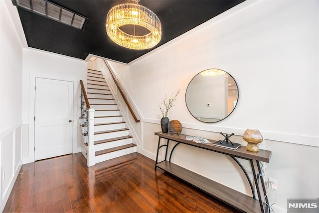 stairway with a decorative wall, a notable chandelier, and wood finished floors