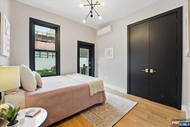 bedroom featuring wood finished floors, a notable chandelier, an AC wall unit, and baseboards