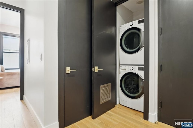clothes washing area featuring stacked washing maching and dryer, light wood-type flooring, visible vents, and laundry area