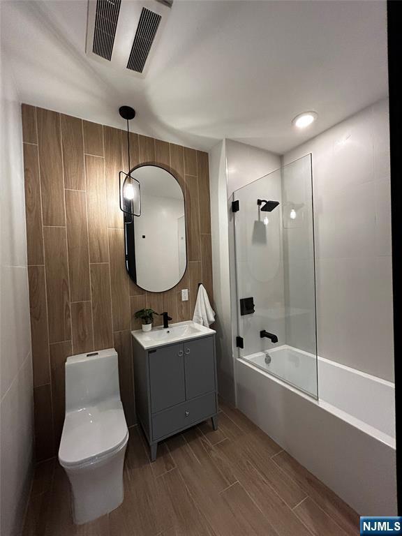 full bathroom featuring vanity, shower / tub combination, toilet, visible vents, and tile walls