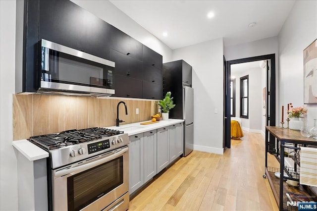 kitchen with a sink, light countertops, light wood-type flooring, and stainless steel appliances