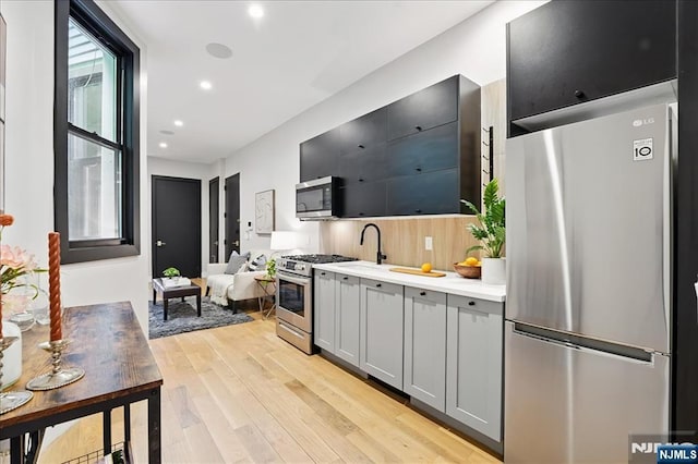 kitchen with light wood-type flooring, recessed lighting, appliances with stainless steel finishes, light countertops, and gray cabinetry