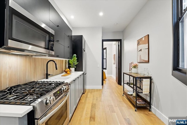 kitchen with light wood-type flooring, baseboards, dark cabinetry, and appliances with stainless steel finishes