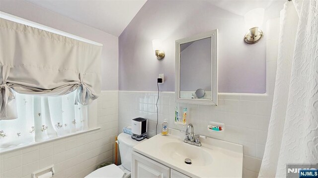 bathroom featuring tile walls, a wainscoted wall, toilet, and vanity