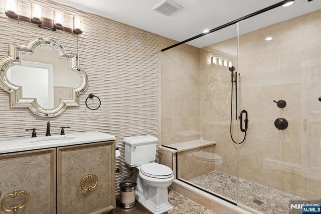 full bath with vanity, toilet, tile walls, visible vents, and tiled shower