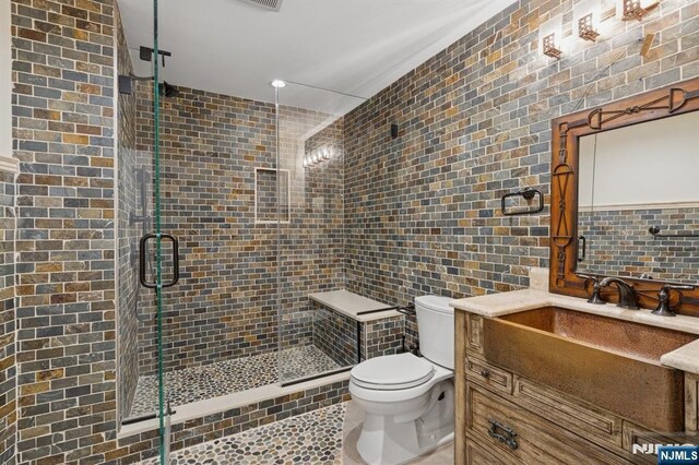 bathroom featuring tile walls, tasteful backsplash, a shower stall, vanity, and toilet