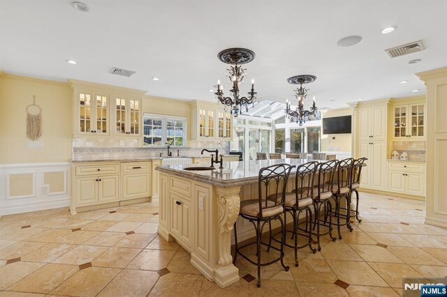 kitchen featuring visible vents, a kitchen breakfast bar, a chandelier, cream cabinetry, and a sink