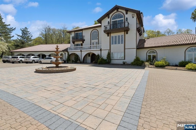 view of front facade featuring curved driveway, stucco siding, a balcony, and a tiled roof