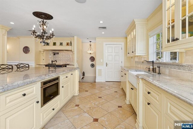 kitchen with visible vents, light stone counters, cream cabinetry, and tasteful backsplash