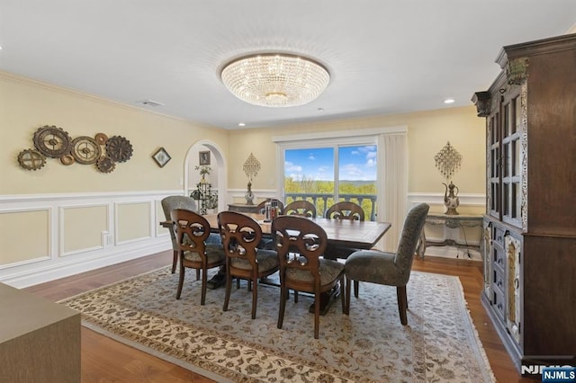 dining space featuring an inviting chandelier, ornamental molding, wainscoting, and dark wood-style floors