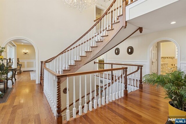 staircase with a high ceiling, an inviting chandelier, a decorative wall, arched walkways, and wood finished floors