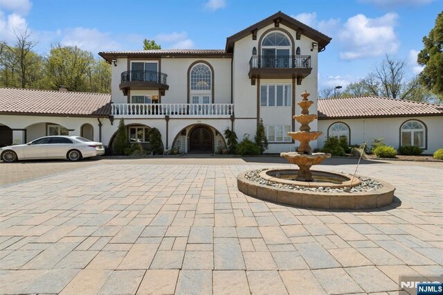 mediterranean / spanish-style house featuring curved driveway, stucco siding, a balcony, and a tile roof