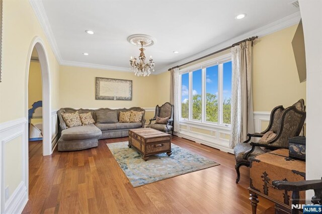 living area with crown molding, a wainscoted wall, arched walkways, and wood finished floors