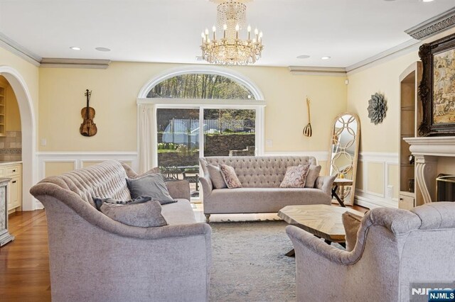 living area featuring an inviting chandelier, wainscoting, arched walkways, wood finished floors, and ornamental molding