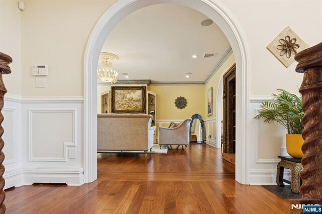corridor featuring arched walkways, a decorative wall, wood finished floors, and visible vents