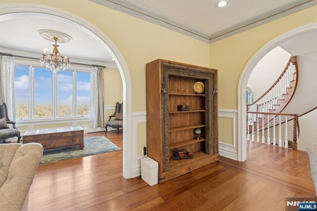 interior space with arched walkways, wood finished floors, a notable chandelier, and a wainscoted wall