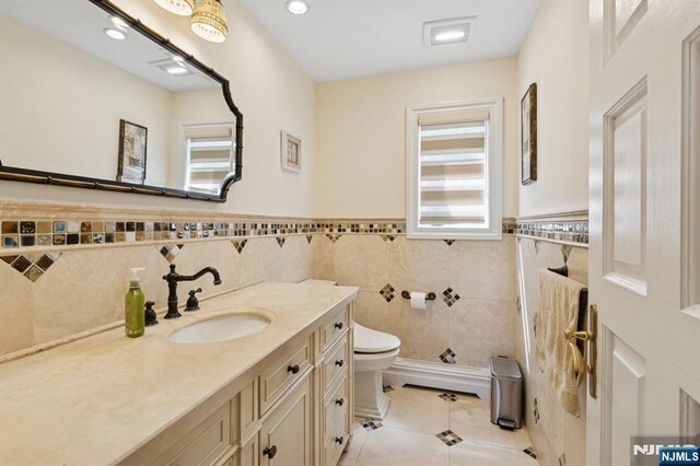 bathroom with vanity, wainscoting, toilet, tile walls, and tile patterned floors