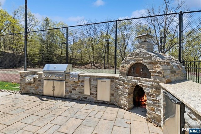view of patio with fence, area for grilling, and an outdoor stone fireplace