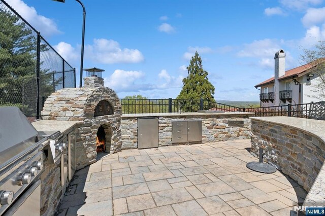 view of patio featuring an outdoor stone fireplace, fence, and an outdoor kitchen