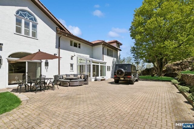 rear view of property with a tiled roof, a patio, stucco siding, and outdoor lounge area
