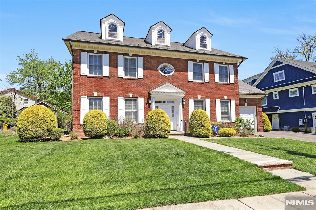 321 Rutland Ave, Teaneck, NJ 07666 - colonial-style house featuring brick siding, an attached garage, driveway, and a front lawn