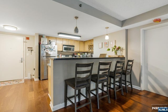 kitchen featuring a peninsula, wood finished floors, dark countertops, appliances with stainless steel finishes, and a kitchen breakfast bar