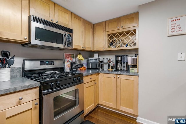 kitchen featuring baseboards, stainless steel appliances, dark countertops, dark wood-type flooring, and light brown cabinets
