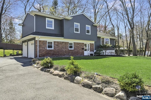 view of front of house featuring aphalt driveway, fence, an attached garage, brick siding, and a front yard