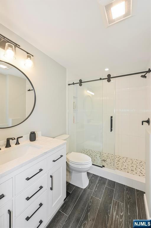 full bathroom featuring toilet, visible vents, wood tiled floor, a shower stall, and vanity