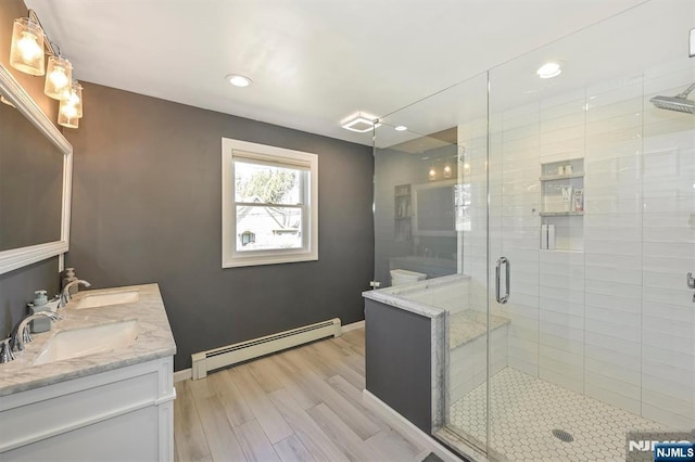 bathroom with baseboard heating, a shower stall, wood finished floors, a sink, and recessed lighting