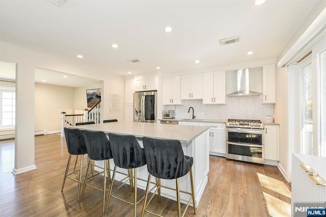 kitchen with backsplash, wall chimney range hood, visible vents, a sink, and appliances with stainless steel finishes