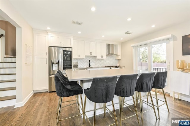kitchen with wood finished floors, stainless steel fridge, white cabinets, wall chimney exhaust hood, and visible vents