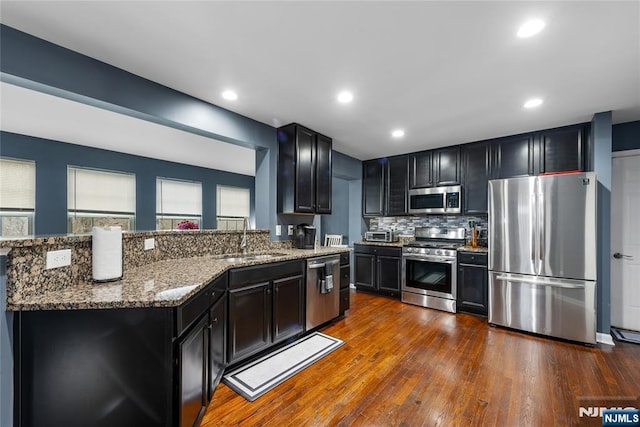 kitchen with stone countertops, dark cabinetry, a sink, and stainless steel appliances