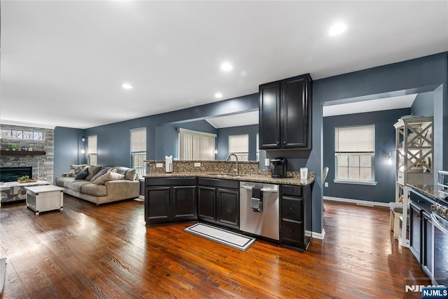 kitchen with a sink, a stone fireplace, dishwasher, and dark wood-style floors