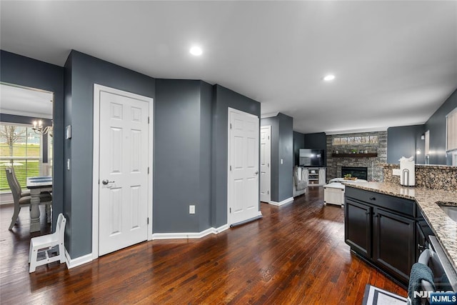 kitchen with an inviting chandelier, a fireplace, dark wood-type flooring, light stone counters, and baseboards