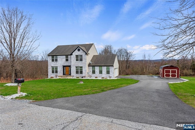 view of front of property with a shed, stone siding, a garage, an outdoor structure, and a front lawn