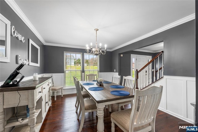 dining area with dark wood-type flooring, wainscoting, an inviting chandelier, and crown molding