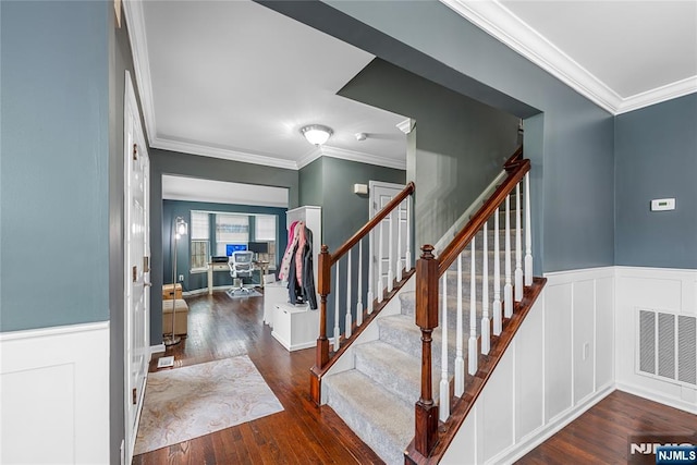 stairs with ornamental molding, visible vents, wainscoting, and wood finished floors