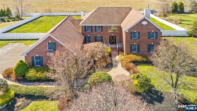 view of front of property featuring brick siding, a front lawn, fence, and a chimney