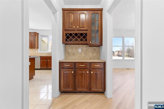 bar with light wood-type flooring, decorative backsplash, and stainless steel dishwasher