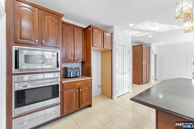 kitchen featuring a warming drawer, appliances with stainless steel finishes, brown cabinetry, and light tile patterned flooring